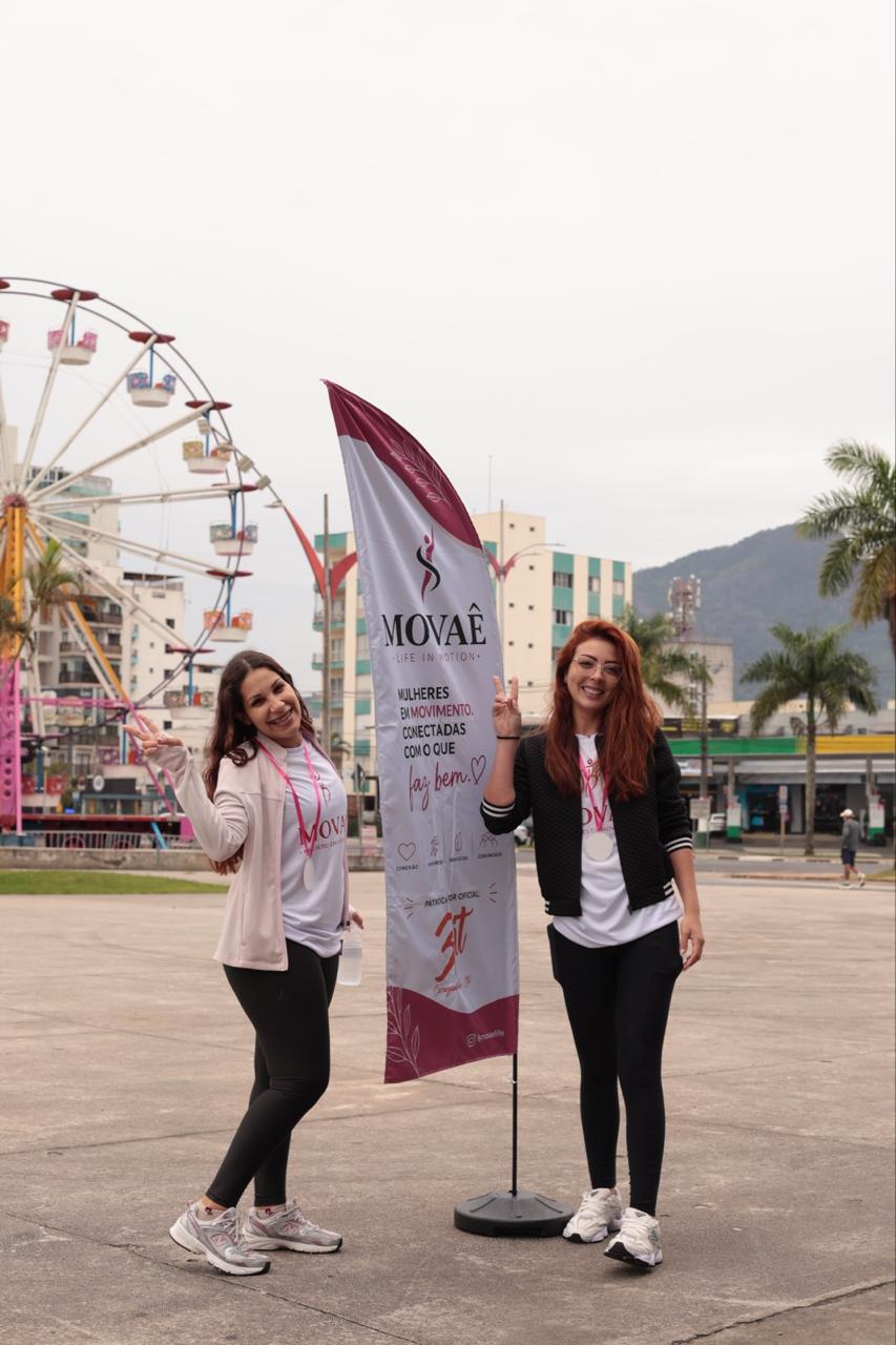 Duas participantes celebrando ao lado da bandeira MOVAÊ