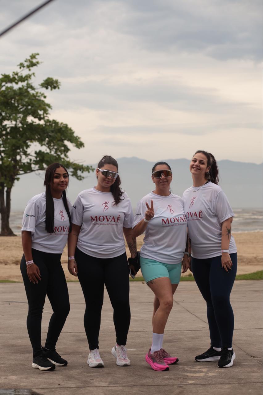 Quatro participantes com camisetas MOVAÊ reunidas à beira-mar